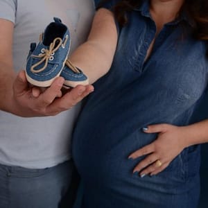 אישה בהריון עם בן זוגה. מחזיקים נעלים כחולות